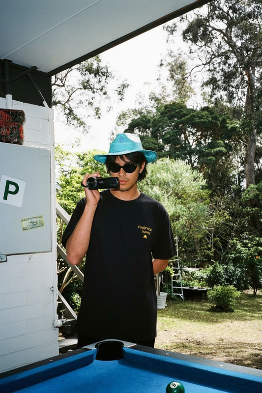 Modelo moreno con la camiseta SNOC Find Your Wave negra en el porche