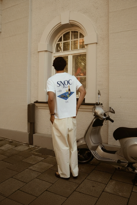 Camiseta Old Wine de SNOC en blanco, vista trasera con el estampado de pista de pádel y vino, llevada en la calle junto a una Vespa