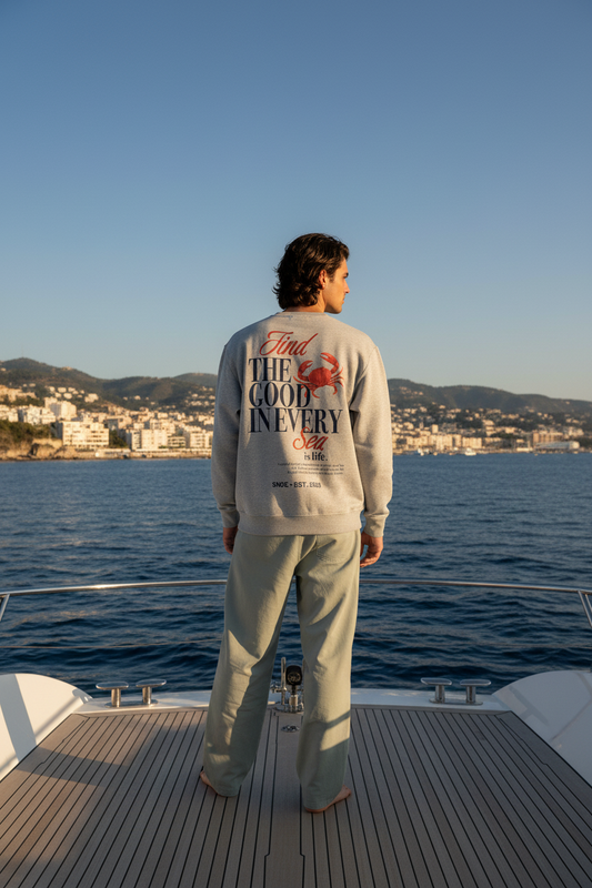 Sudadera Crab and Sea de SNOC vista por la espalda con el cangrejo rojo sobre el logo, junto a un yate