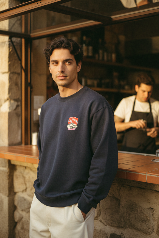 Chico con la sudadera SNOC Por Favor, vista frontal con el sombrero vaquero en el pecho, en un café