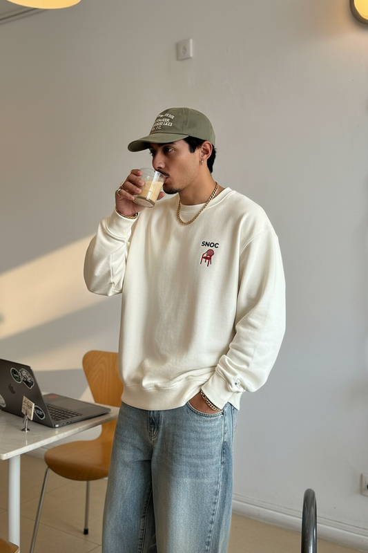 Sudadera Take a Seat de SNOC en blanco con la silla roja estampada en el pecho, llevada en el interior de un café